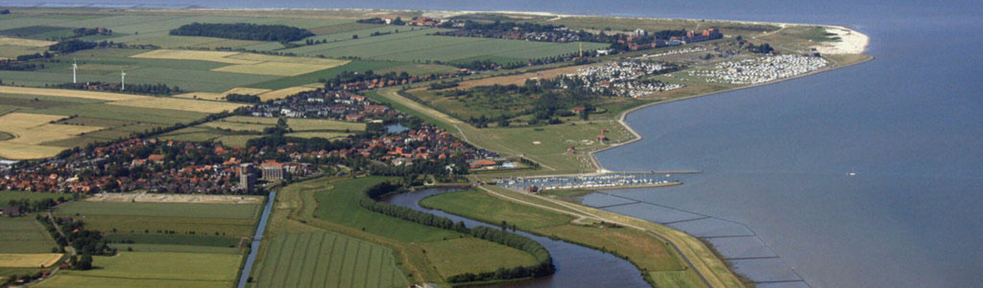 Aerial of diked coasline with sea on the right and beach, settlements and green fields on left.