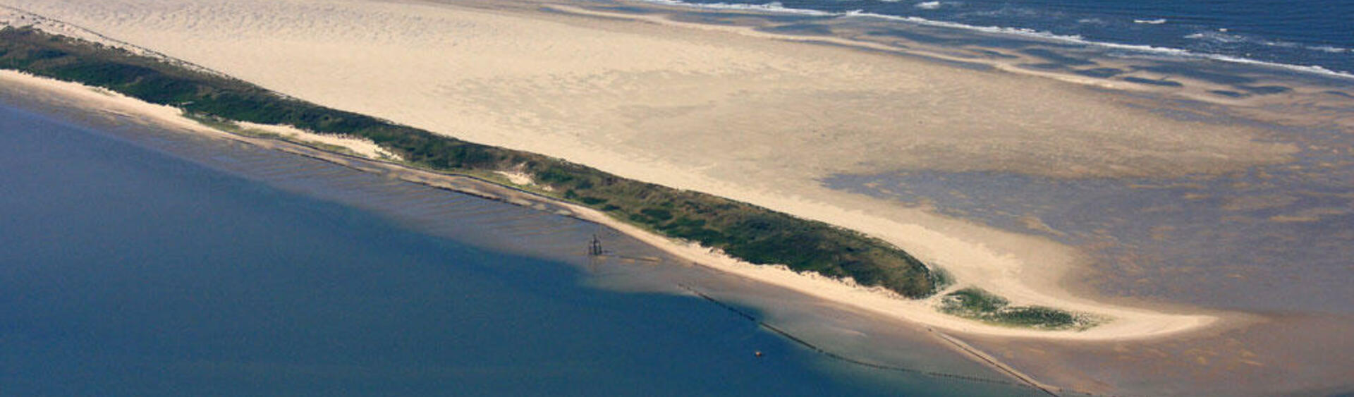 Aerial picture of long-streched sandy dune island wiht green vegetation and wide beach.