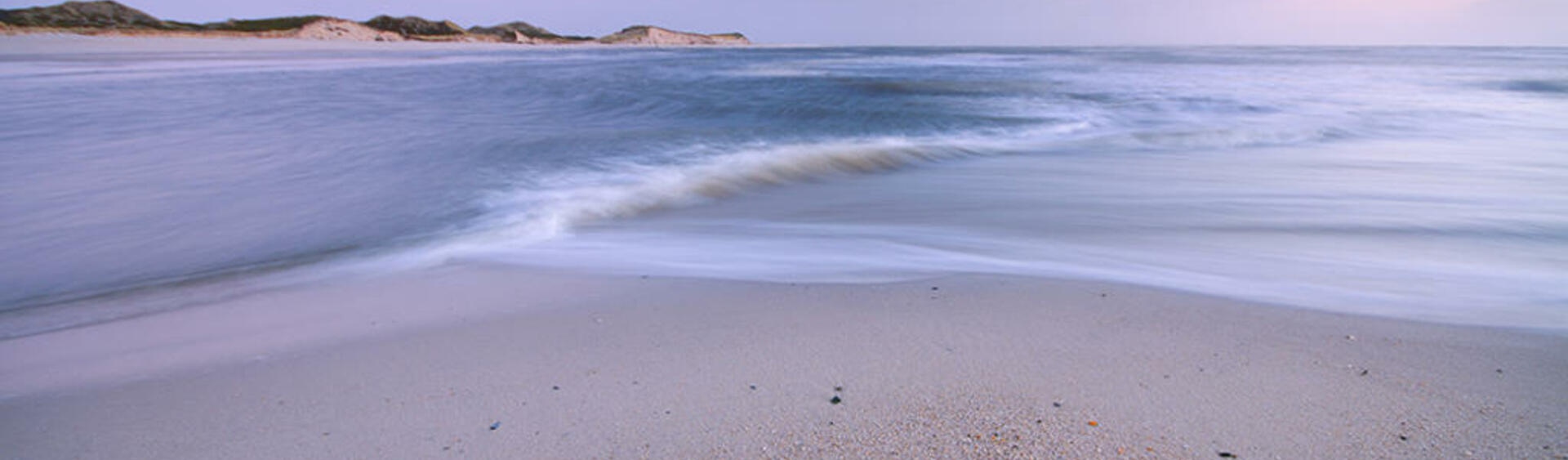 Picture of shoreline on a beach taken from low angle close to the waves with dunes on the horizon. © A. Schnabler