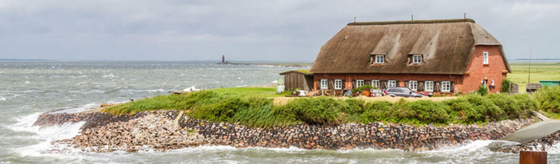 Reet-covered red-brick house on a small patch of land surrounded by stormy waters. © Martin Stock