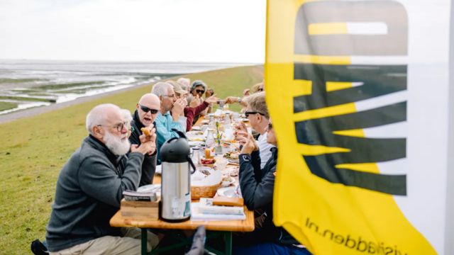 Group of people sitting on a long breakfast table on a dyke. © Marleen Annema.